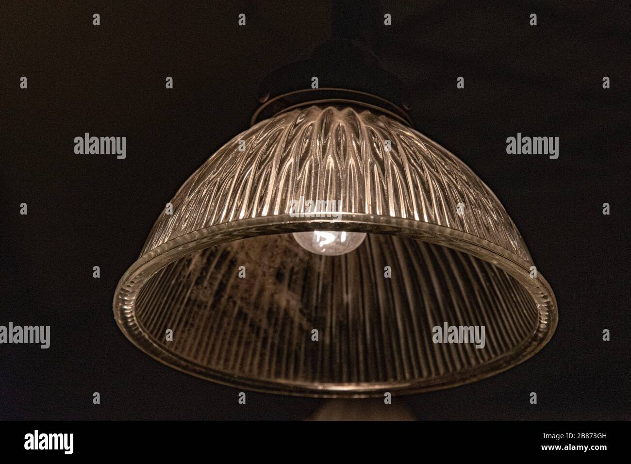 Vintage ornate glass lampshade closeup on black background. Ribbed surface of transparent glass lamp with light bulb inside. Antique pendant light Stock Photo