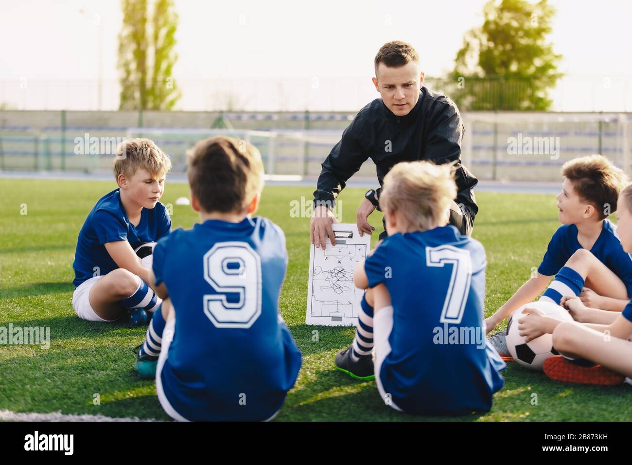 Young coach teaching kids on football field. Football coach coaching