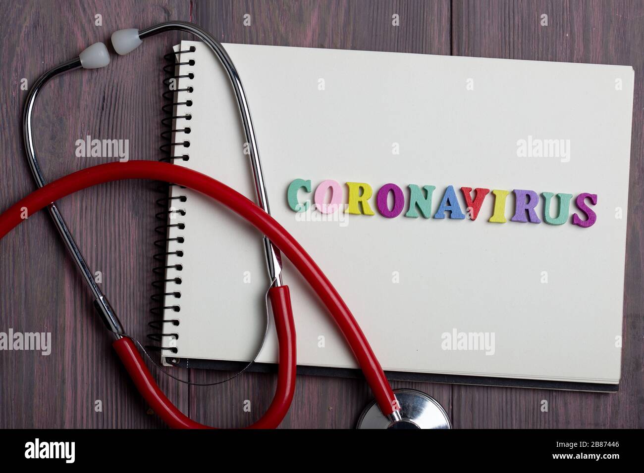 Text Coronavirus wooden letters on notebook and stethoscope on wooden background - healthcare and medical concept Stock Photo