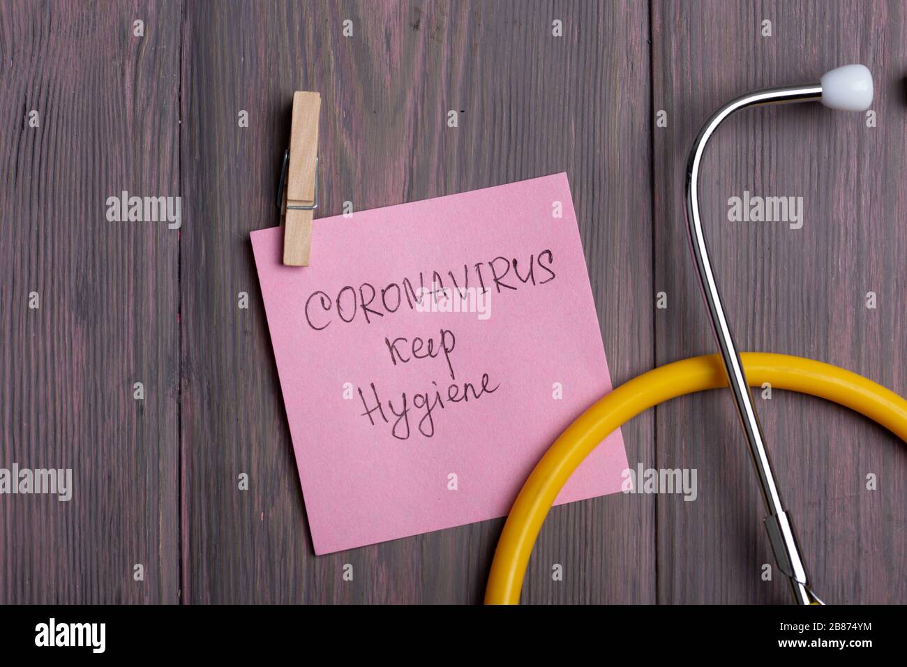 Text Coronavirus keep hygiene on sticky note that hangs with a clothespin and stethoscope on wooden background - healthcare and medical concept Stock Photo