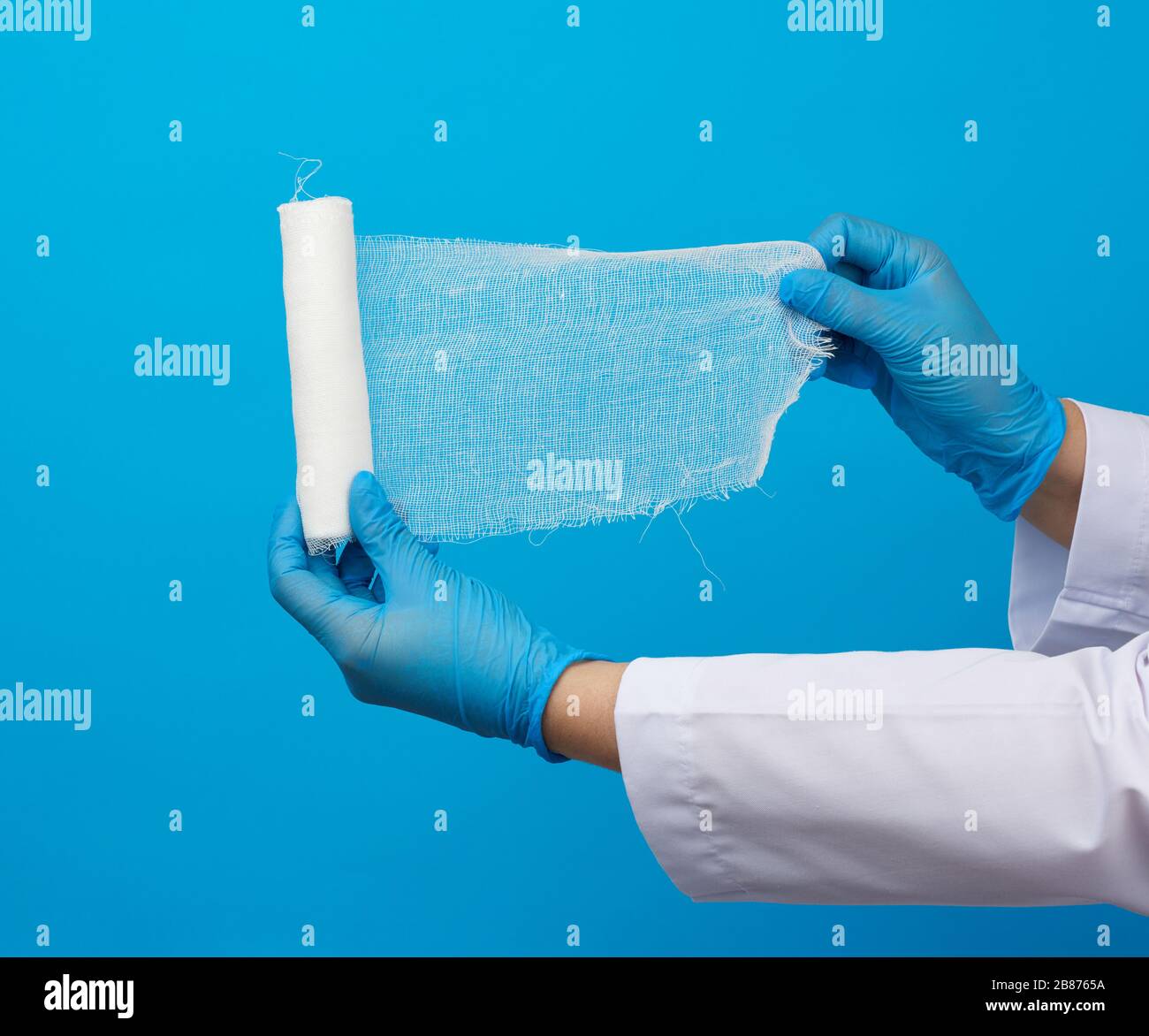 medic woman in white coat holds a twisted gauze bandage, blue background, medical item for bandaging human limbs Stock Photo