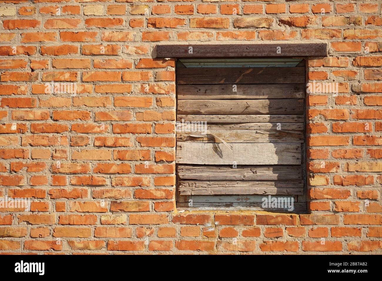Boarded up with wooden planks window opening in an old red brick wall ...