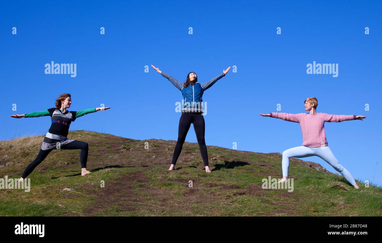 Holyrood Park, Edinburgh, Scotland, UK. 20th Mar 2020. Sunny, and temperature of 6 degrees centigrade, encourages these young ladies to (with appropriate space) take some time out to breathe and meditate while practising Yoga excercises in the cool but fresh air, ensuring to keep their social distance from each other. Pictured: left to right, Jennifer, Belinda and tutor Anna from WanderWomen Scotand. Stock Photo