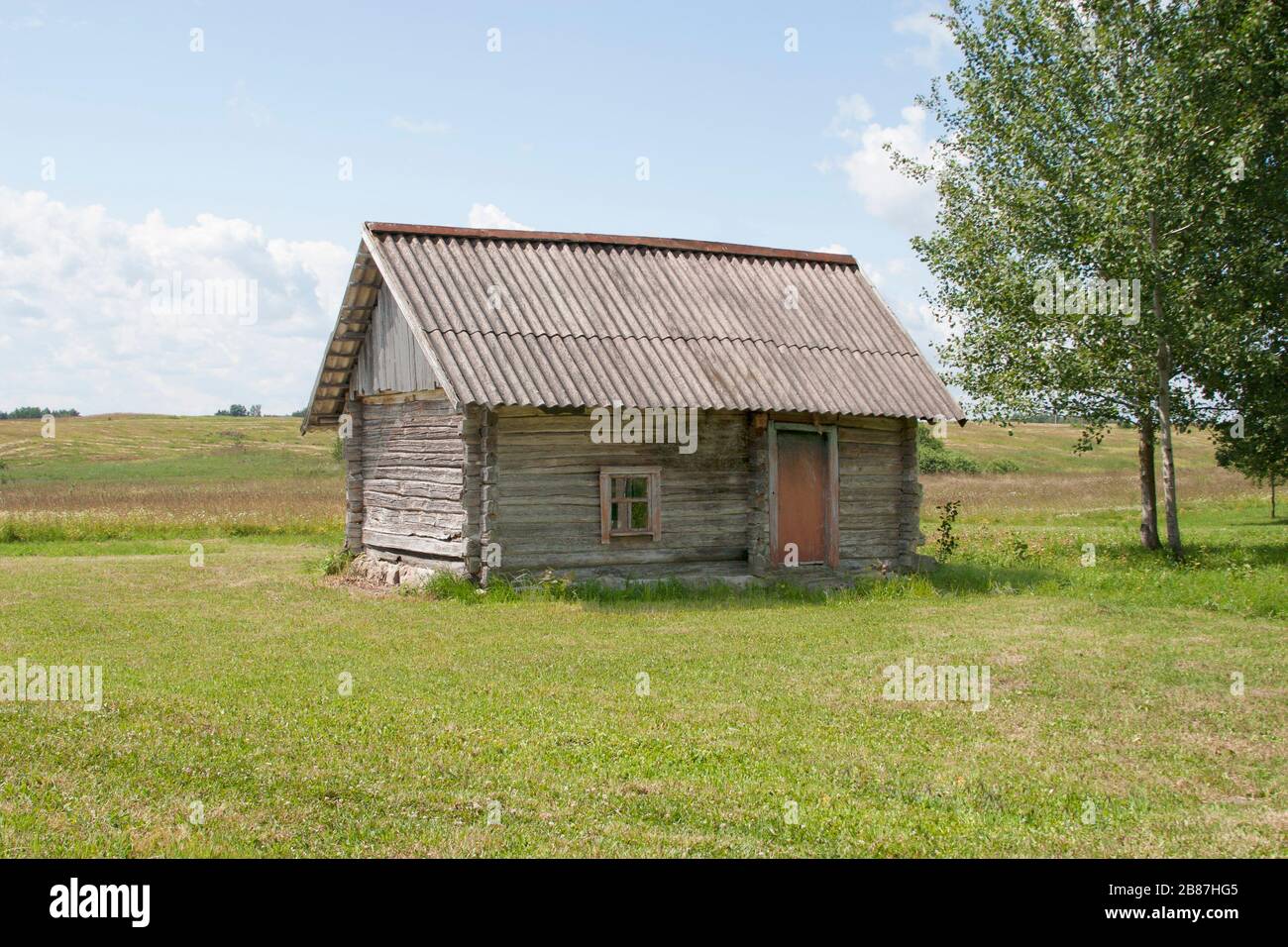 small little old wooden raster log hut in the middle field near by birch tree Stock Photo