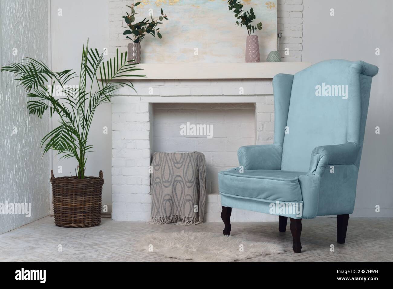 Blue armchair and indoor plants and fireplace in the background. Classical living room furniture and potted plants Stock Photo
