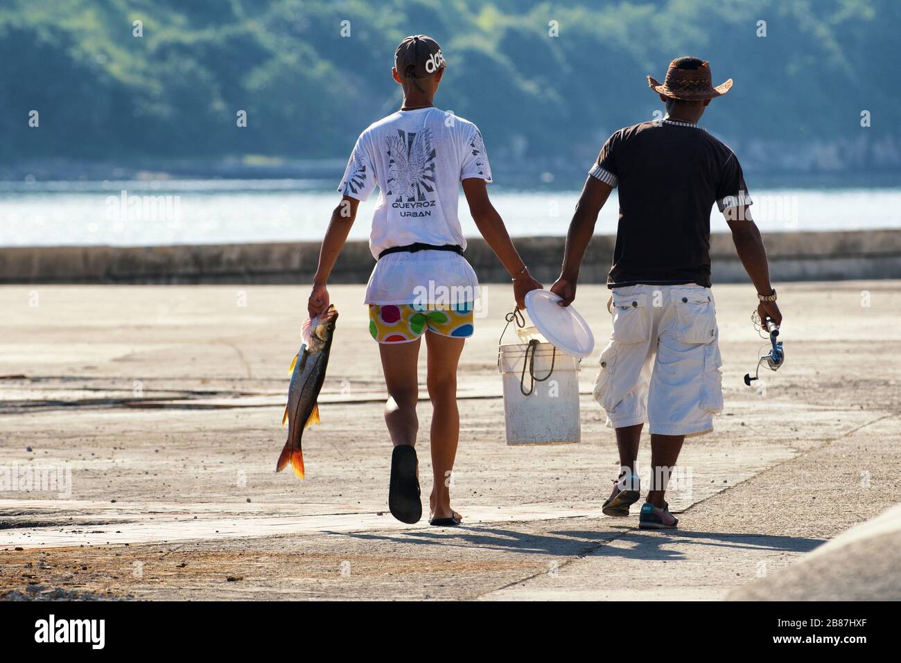 Two fishermen on the Havana waterfront carrying a sea bass fish. Cuban people image. Stock Photo