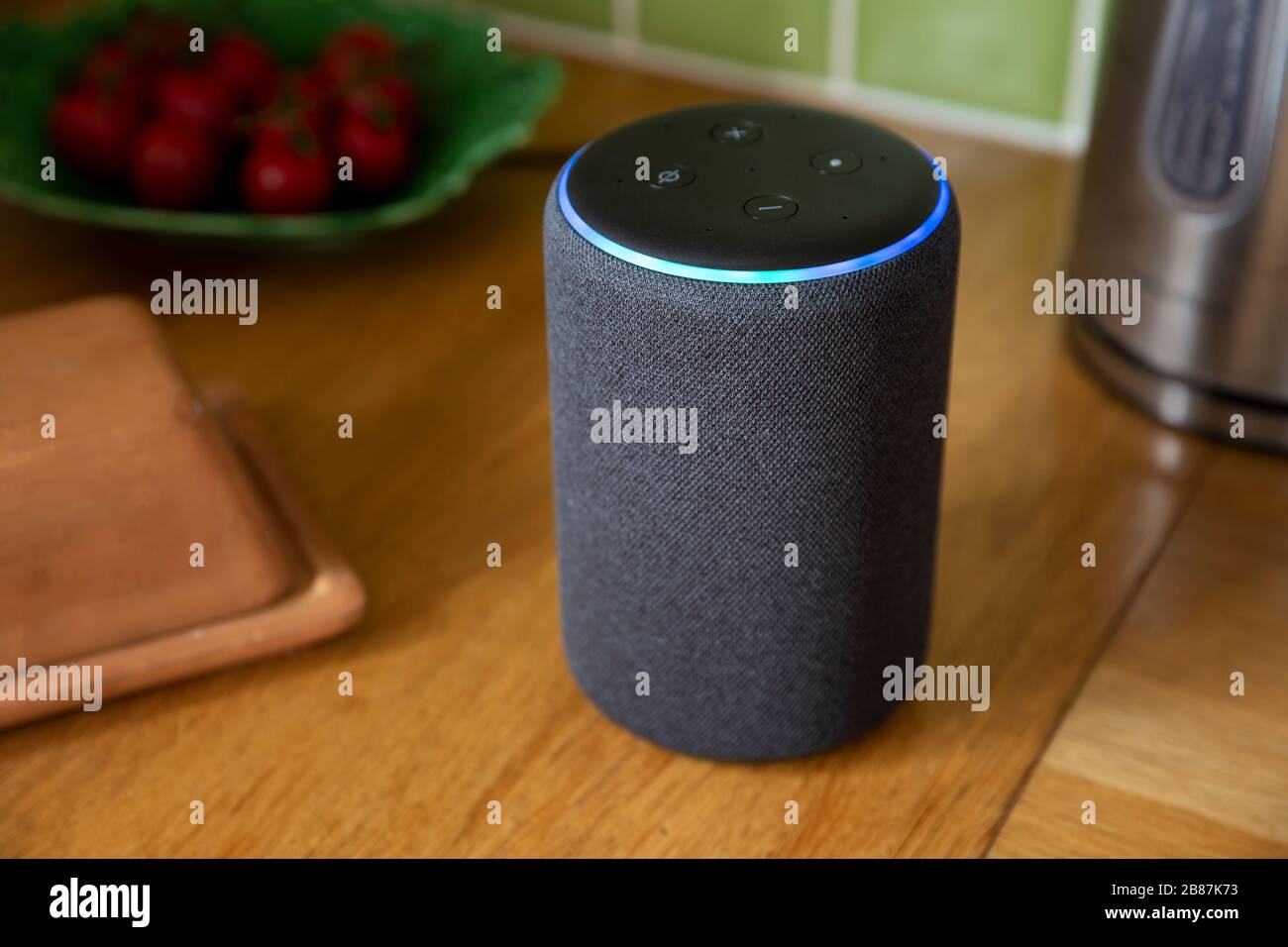BATH, UK - MARCH 20, 2020 : Close up of a 3rd generation Amazon Echo smart speaker glowing blue on a kitchen worktop Stock Photo