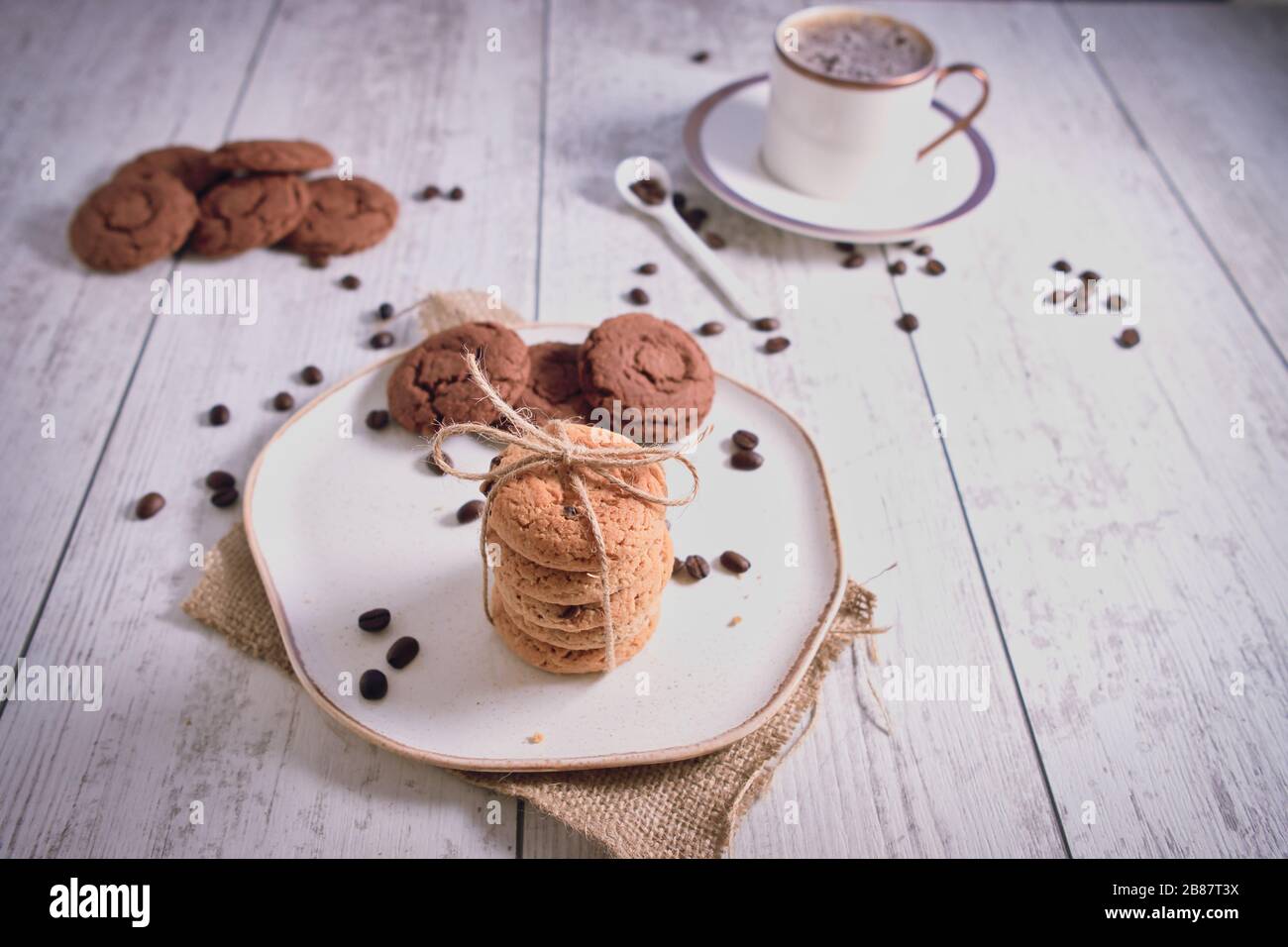 Roasted brown coffee beans and Hot coffee. Beautifully stacked cookies with chocolate on Wooden table. Chocolate chip cookies Vintage Color. Stock Photo