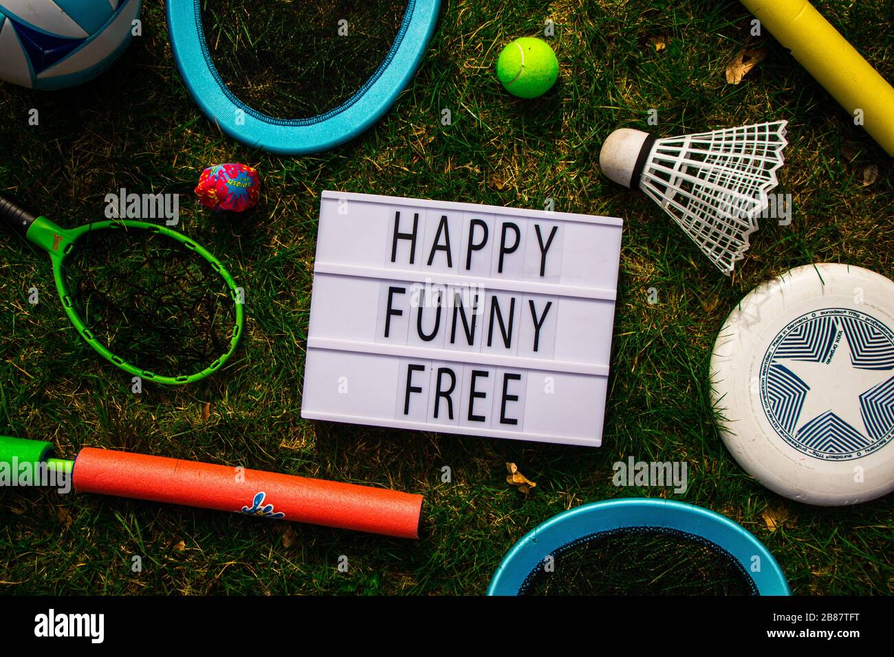 Top down view of a lightbox surrounded by outdoor toys. The lightbox spells: 'Happy Funny Free'. Lifestyle, outside, background, summer, happy. Stock Photo