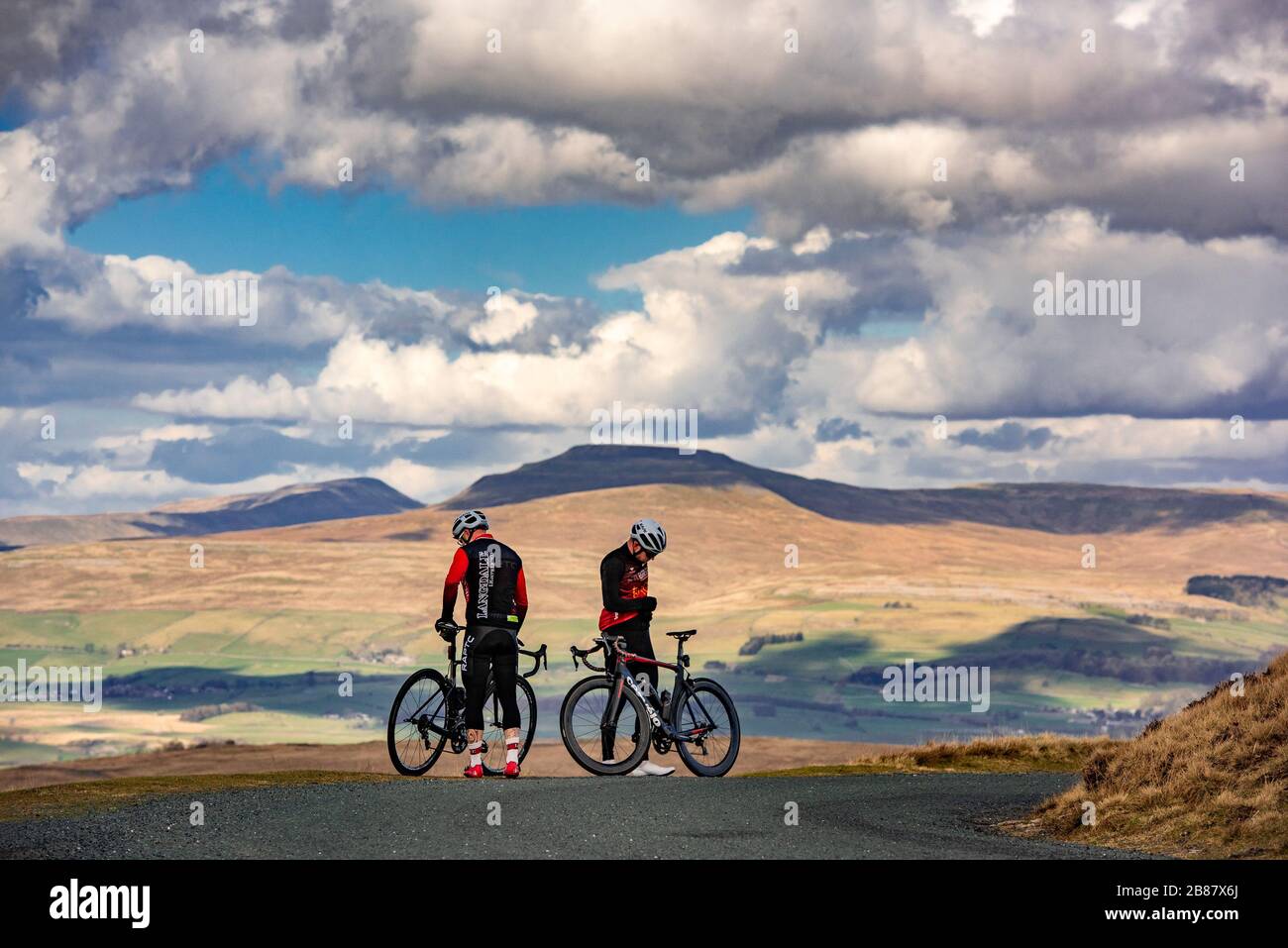 Ingleton, North Yorkshire. 20th March 2020 Two cyclists enjoying the fine weather with Ingleborough Fell, Ingleton, North Yorkshire in the background. Credit: John Eveson/Alamy Live News Stock Photo