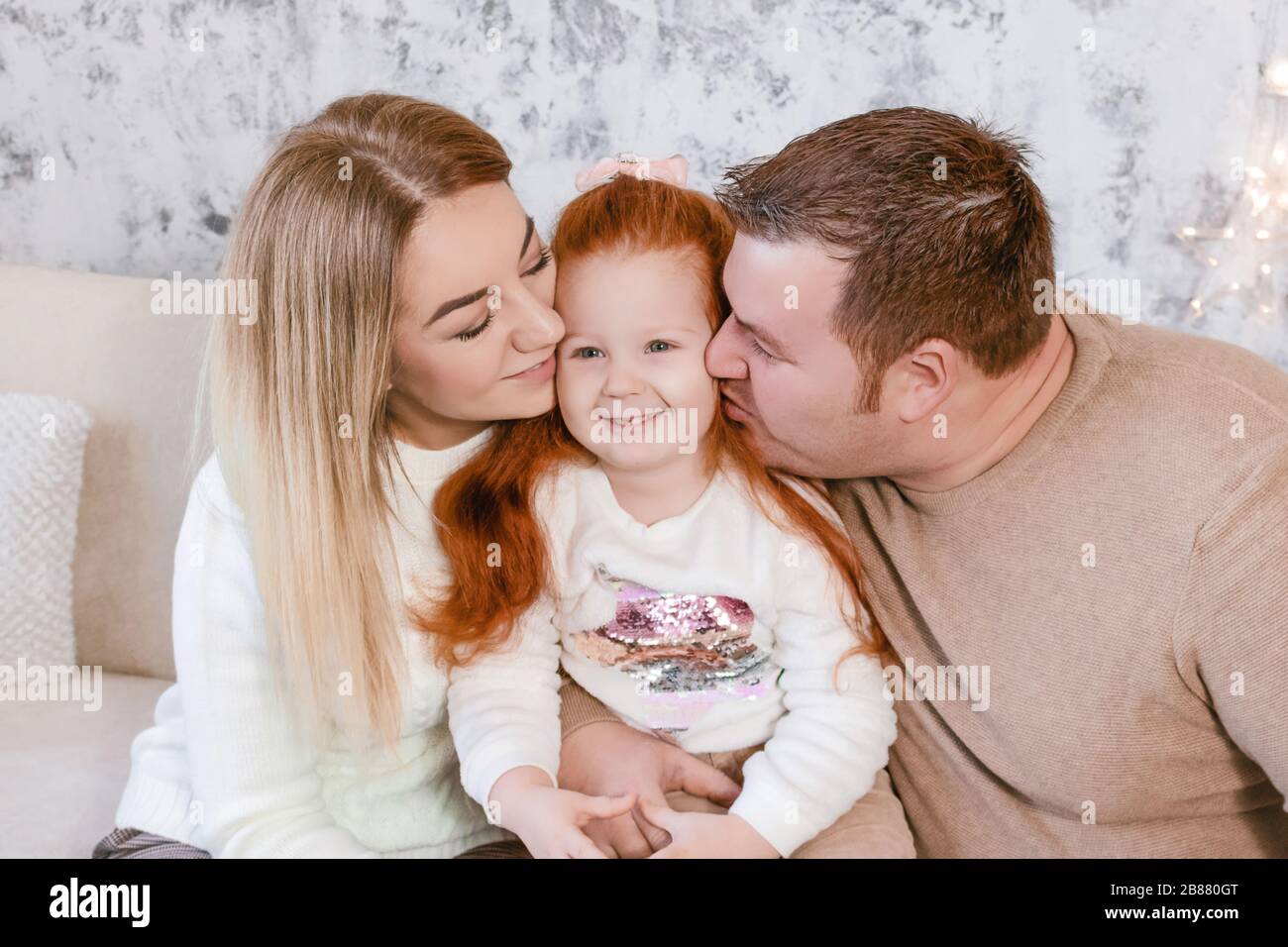 Young parents kissing their daughter in christmas Stock Photo