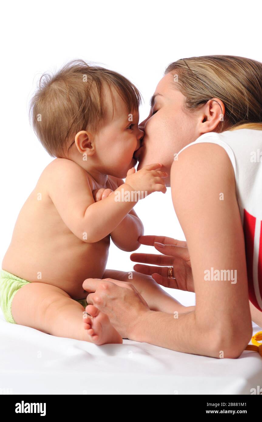 Loving mother kisses pretty little baby girl. Parental love and care. Parent and child portrait on isolated white background Stock Photo