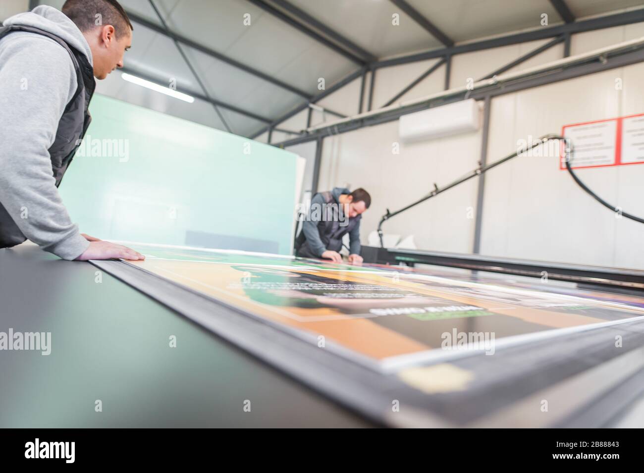 Two printshop worker technicians works on large CNC computer numerical control printing and cutting machine Stock Photo