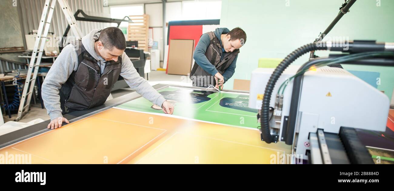 Two printshop worker technicians works on large CNC computer numerical control printing and cutting machine Stock Photo