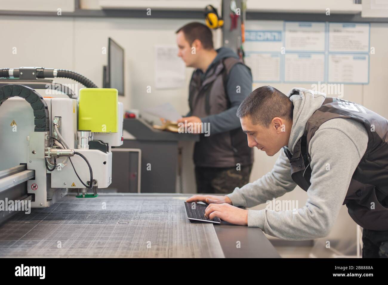 Two printshop worker technicians works on large CNC computer numerical control printing and cutting machine Stock Photo