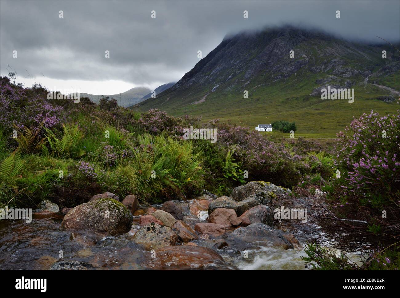 Little white house and creek below Buachaille Etive Mòr, in Glencoe Valley, in the Scottish Highlands in Scotland. Stock Photo