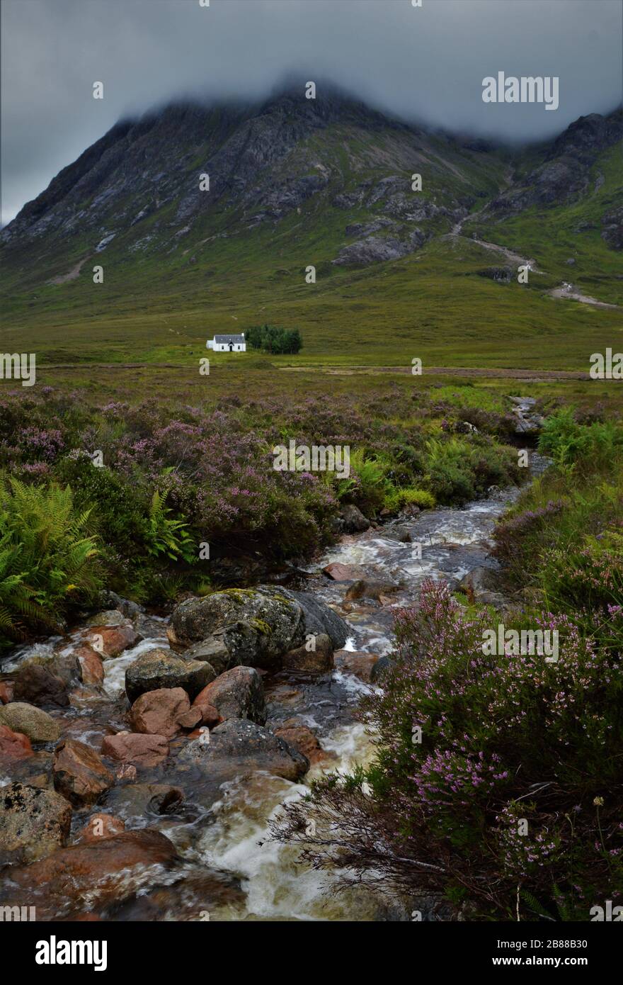 Little white house and creek below Buachaille Etive Mòr, in Glencoe Valley, in the Scottish Highlands in Scotland. Stock Photo