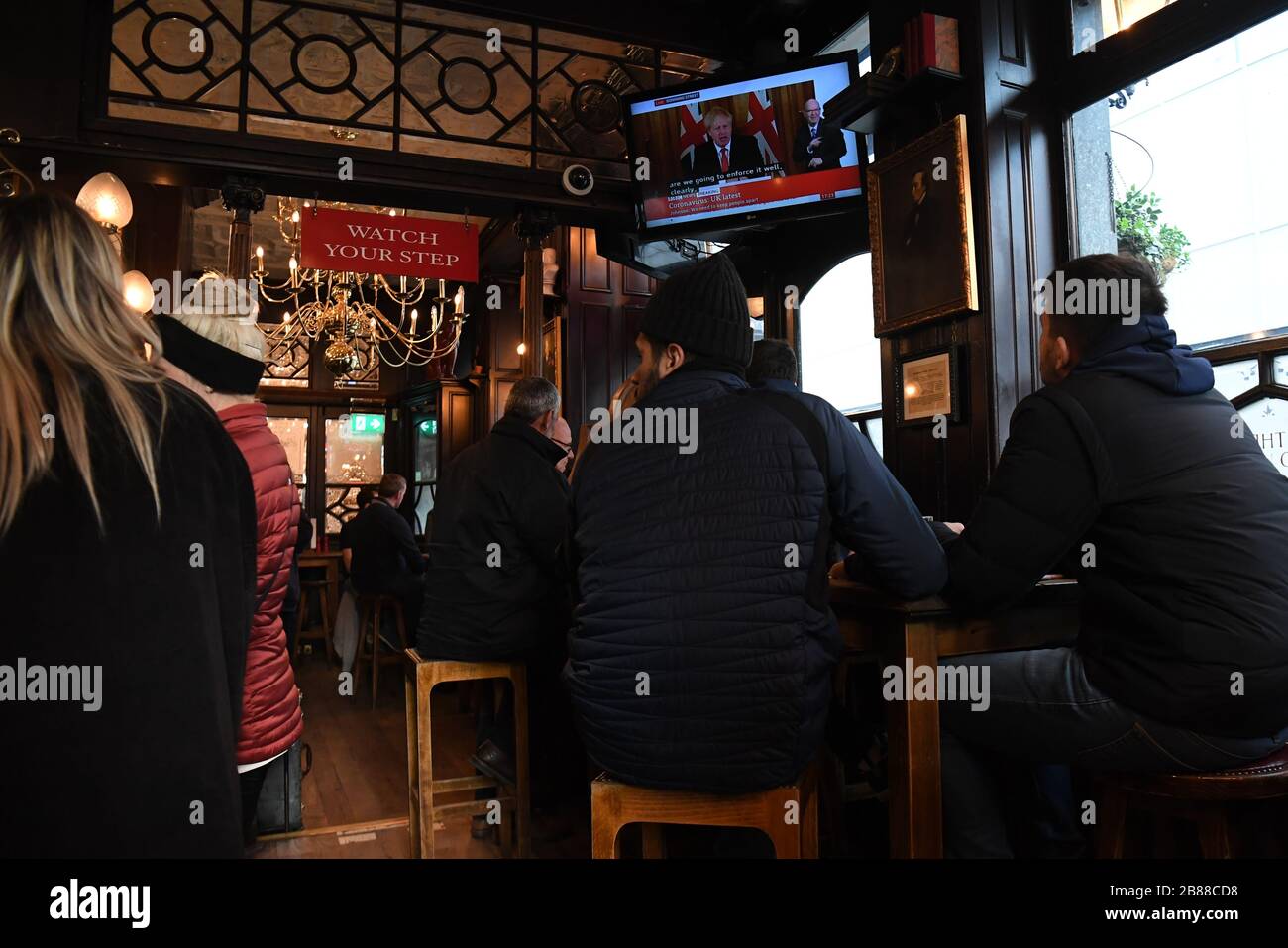 Customers in the Red Lion pub in Westminster in London watch the television as Boris Johnson orders pubs and restaurants across the country to close tonight as the Government announced unprecedented measures to cover the wages of workers who would otherwise lose their jobs due to the coronavirus outbreak. Stock Photo