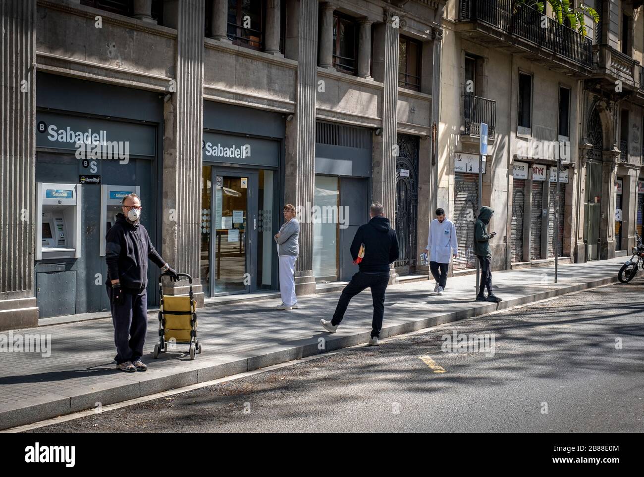 Several people wait in front of a bank while keeping safe distance due to the spread of the coronavirus.Barcelona faces the sixth consecutive day of home confinement and distancing between people due to the spread of the Covid-19 coronavirus. Stock Photo