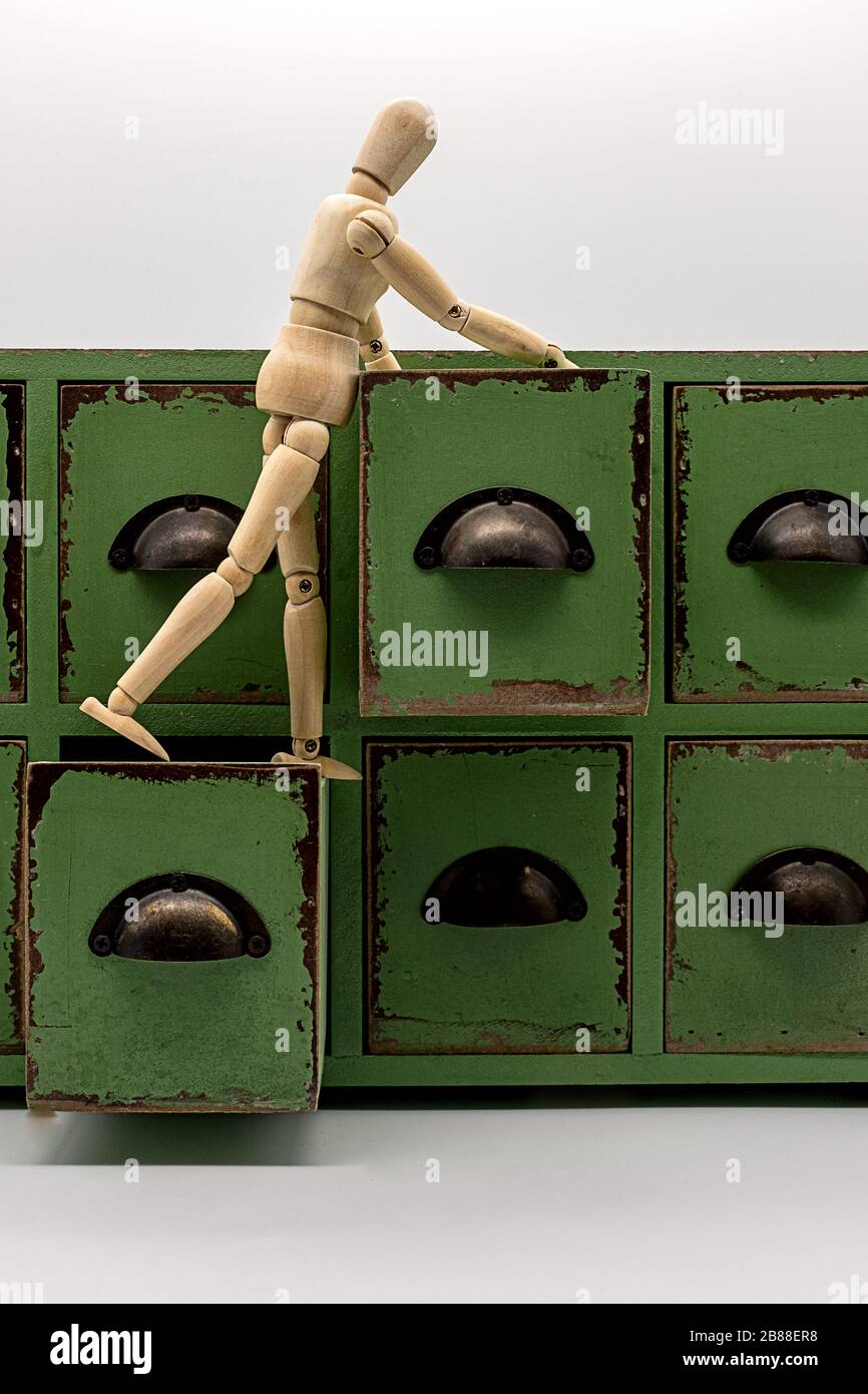 a wooden doll stands on two open drawers of a small chest of drawers and is looking for something Stock Photo