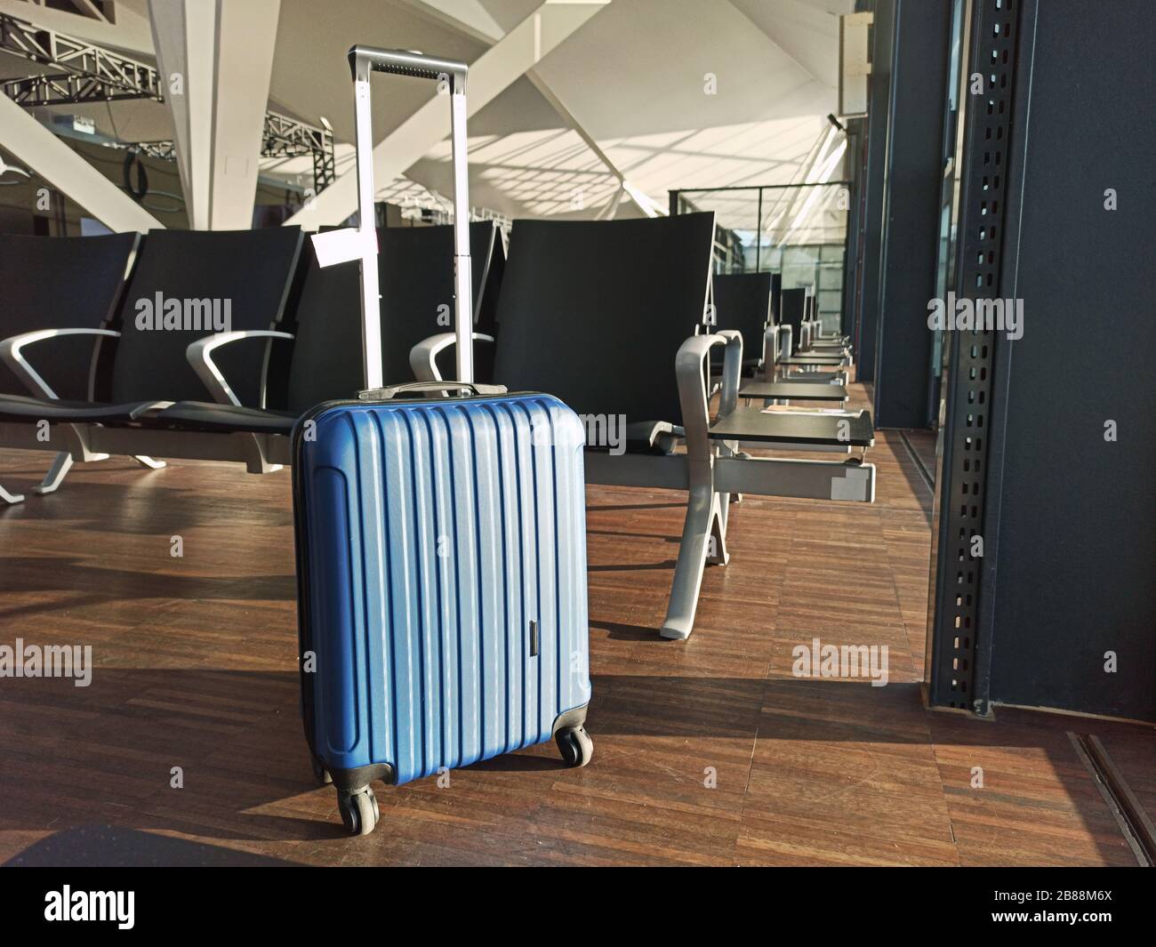 Blue suitcase in an empty airport. Waiting area Flight delay cancellation. Travel and vacation concept. Coronavirus COVID19 quarantine Stock Photo