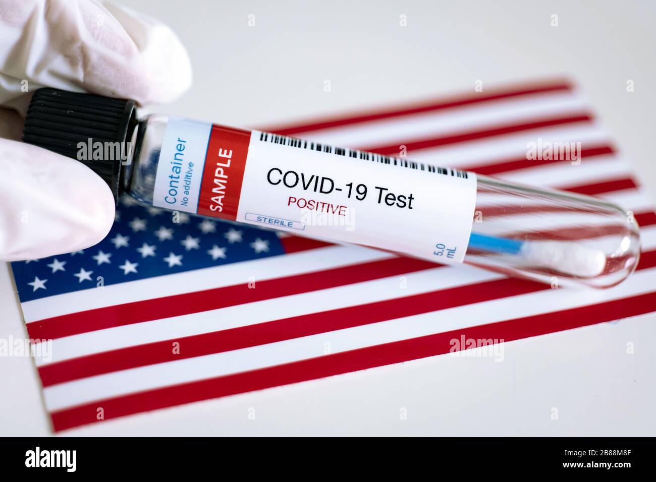Testing for presence of coronavirus. Tube containing a swab sample that has tested positive for COVID-19. Flag of the United States in the background. Stock Photo