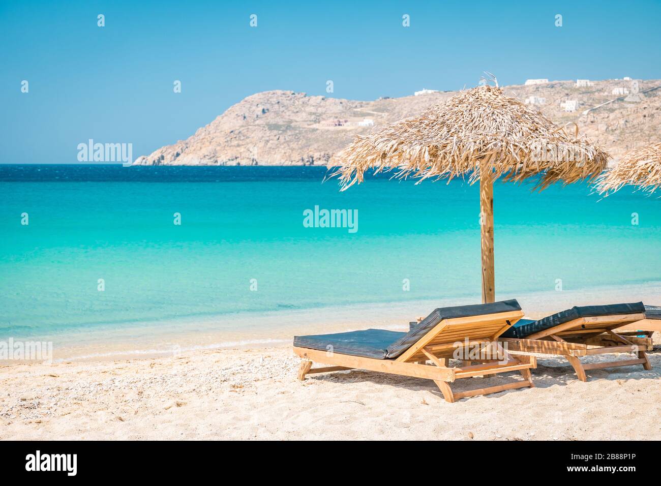 Mykonos beach during summer with umbrella and luxury beach chairs beds, blue ocean with mountain at Elia beach Mikonos Greece Stock Photo