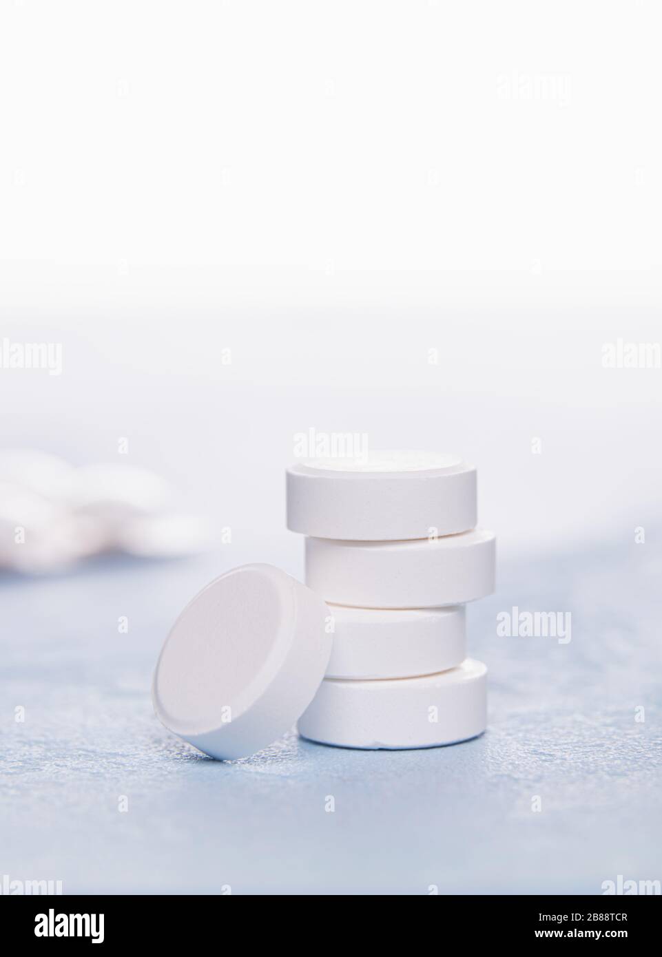 Close-up of large white round tablets of Vitamin C grouped in turret. One tablet is at the bottom of pile. Unfocused blister pack at background. Selec Stock Photo