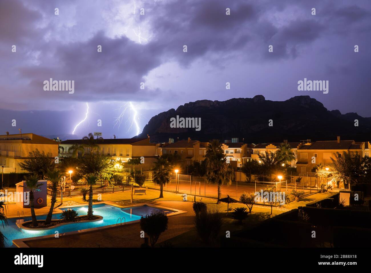 El Verger,Spain-August 27,2019-a lightning strikes from stromy clouds over a village with a pool and mountains Stock Photo