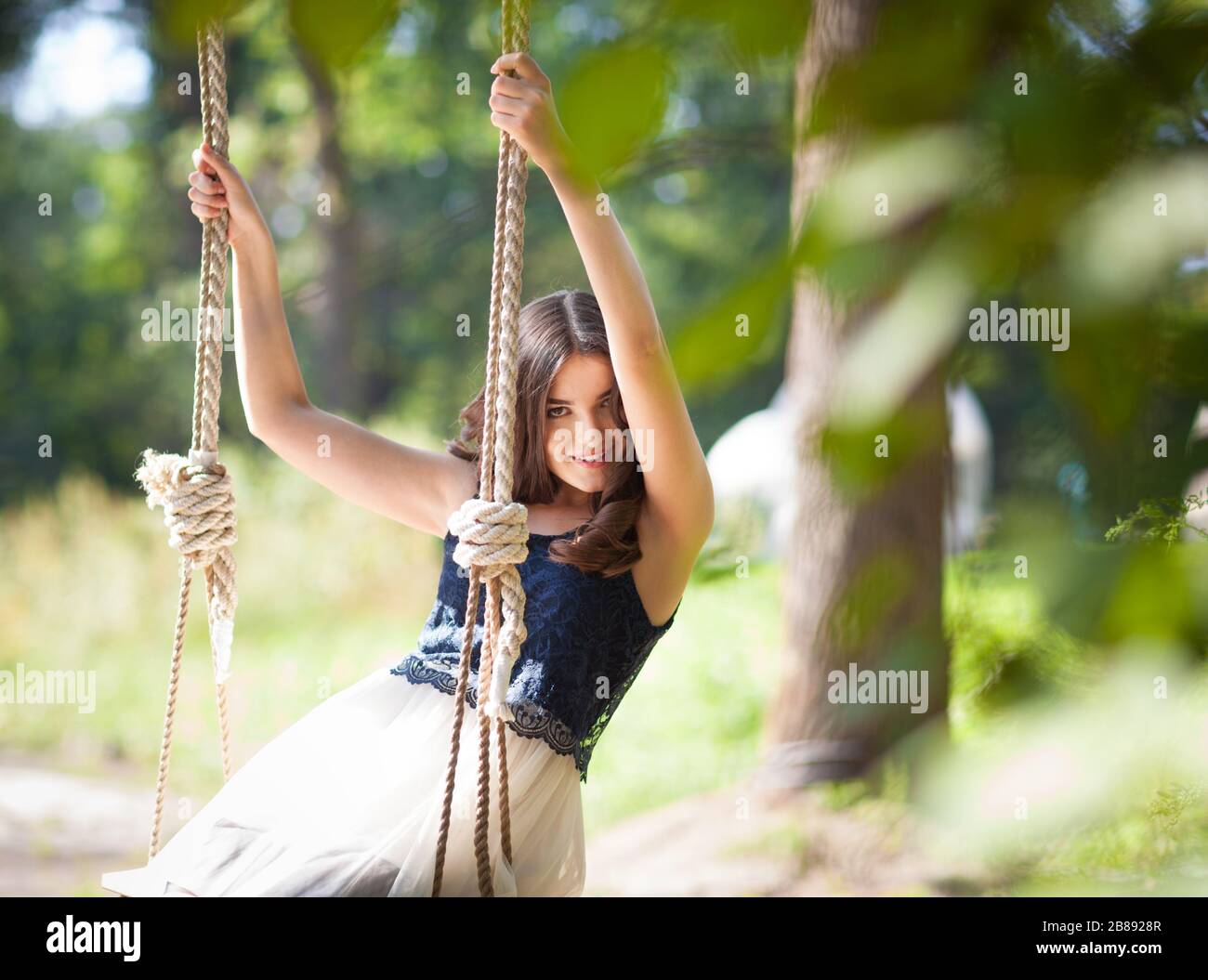 Front view of beautiful elegant lady swinging on hanging swing. Charming  girl in stylish dress holding ropes and looking at camera with cute smile.  Co Stock Photo - Alamy