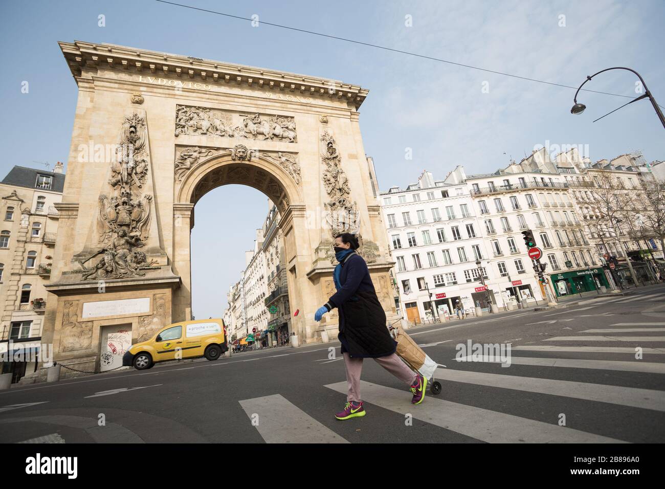 Paris, France. 20th Mar, 2020. A woman walks by a desolate Porte  Saint-Denis arch during the afternoon of March 20, 2020. Paris has been on  lockdown since Tuesday to curb the spread