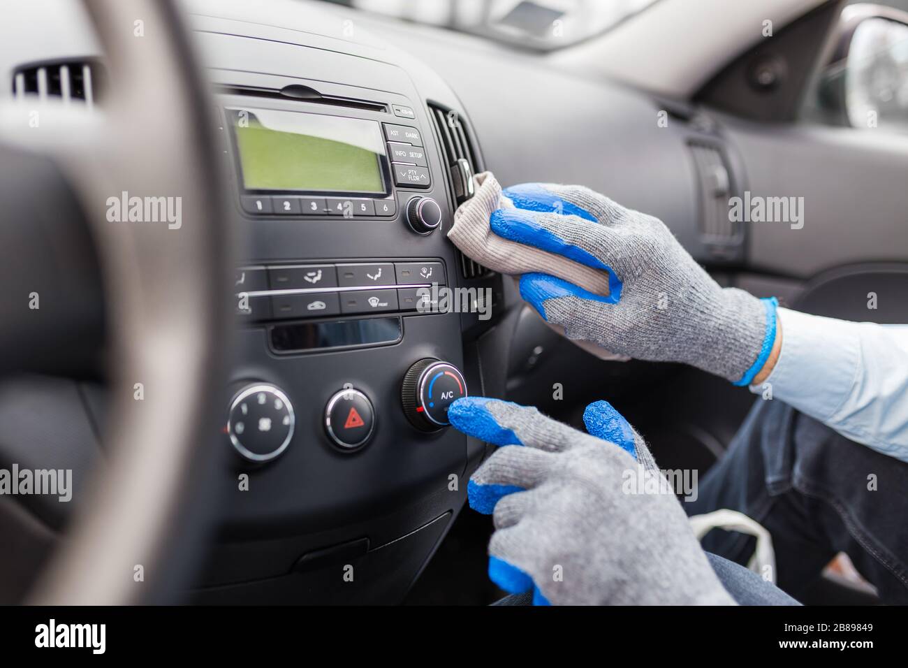 Worker cleaning car interior, pressing ac button and holding microfiber