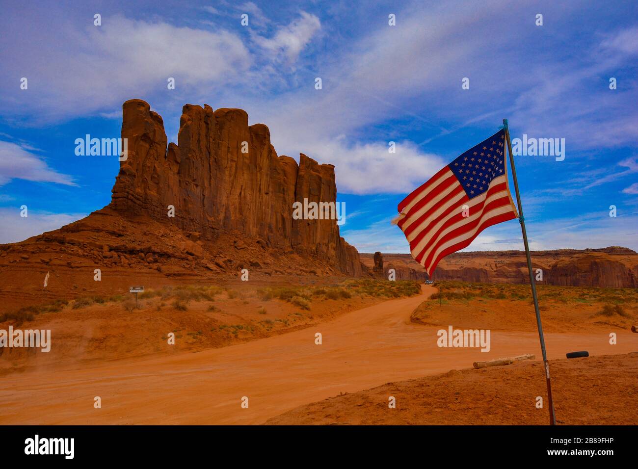 Breathtaking view of the camel butte in Monument Valley. The american flag waves in the blue sky, amazing red rocks and orange dirt road, typical of t Stock Photo