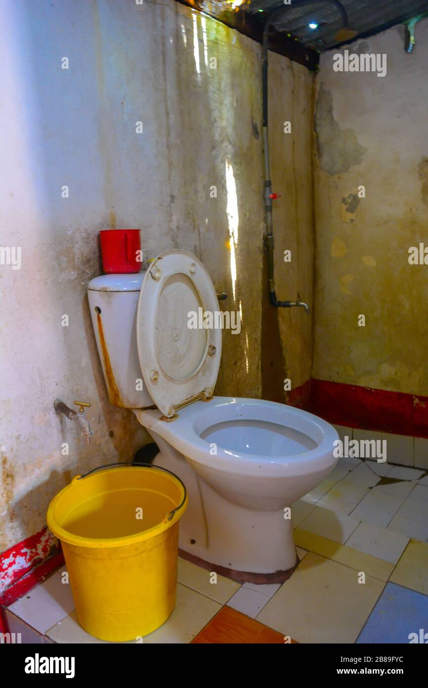 A nightmare bathroom: mold, rusty and dirty toilette, bucket instead of toilet paper, hole in the roof with rain pooring in. Worst hotel bathroom Stock Photo