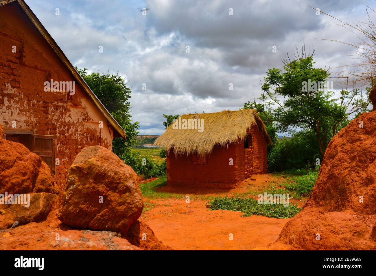 An african orange mudhouse. In a small, remote, madagascan village a basic house with walls made of mud, roof made of straws, dirt road. Cozy home Stock Photo
