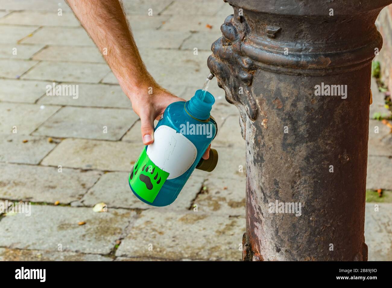 Man filling white blue plastic sport bottle using Old bronze public street tap for fresh water. Traditional drinking water fountain Venice Italy. Stock Photo