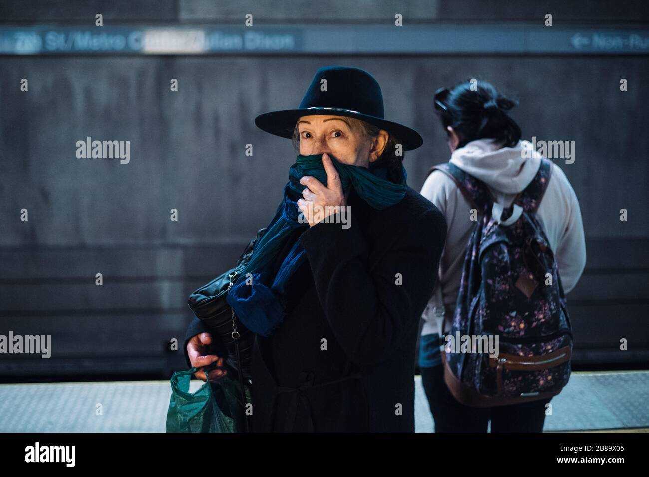 A woman covers her face with a scarf during covid-19 global pandemic mask shortage waiting for metro train in Los Angeles, California Stock Photo