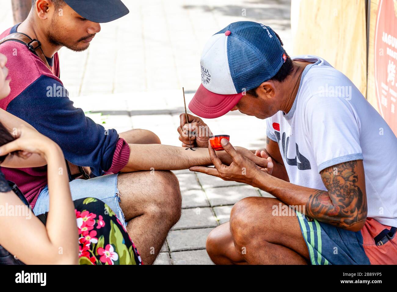 A Local Tattoo Artist Paints A Temporary Henna Tattoo On The Arm Of A Tourist, Tanah Lot Temple, Bali, Indonesia. Stock Photo