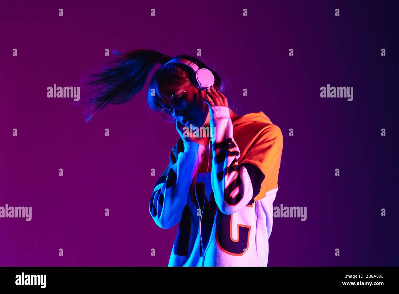 Fashion teenager wearing headphones listening music dancing in purple light. Stock Photo