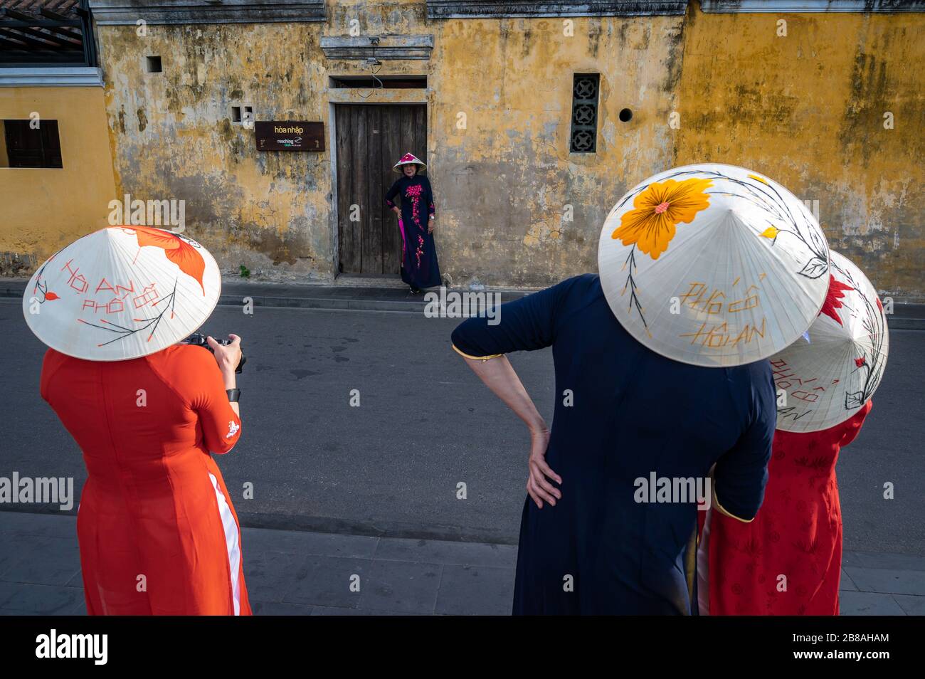 Female tourists in conical hats and traditional clothing taking pictures in Hoi An, Vietnam Stock Photo