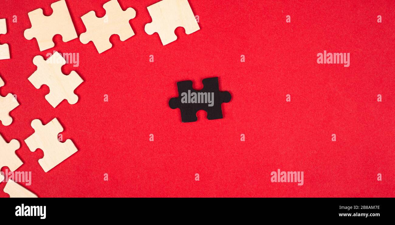 wooden white and black puzzles on a red background close-up top view. outcast antisocial leader differ from others children's educational toy. Stock Photo