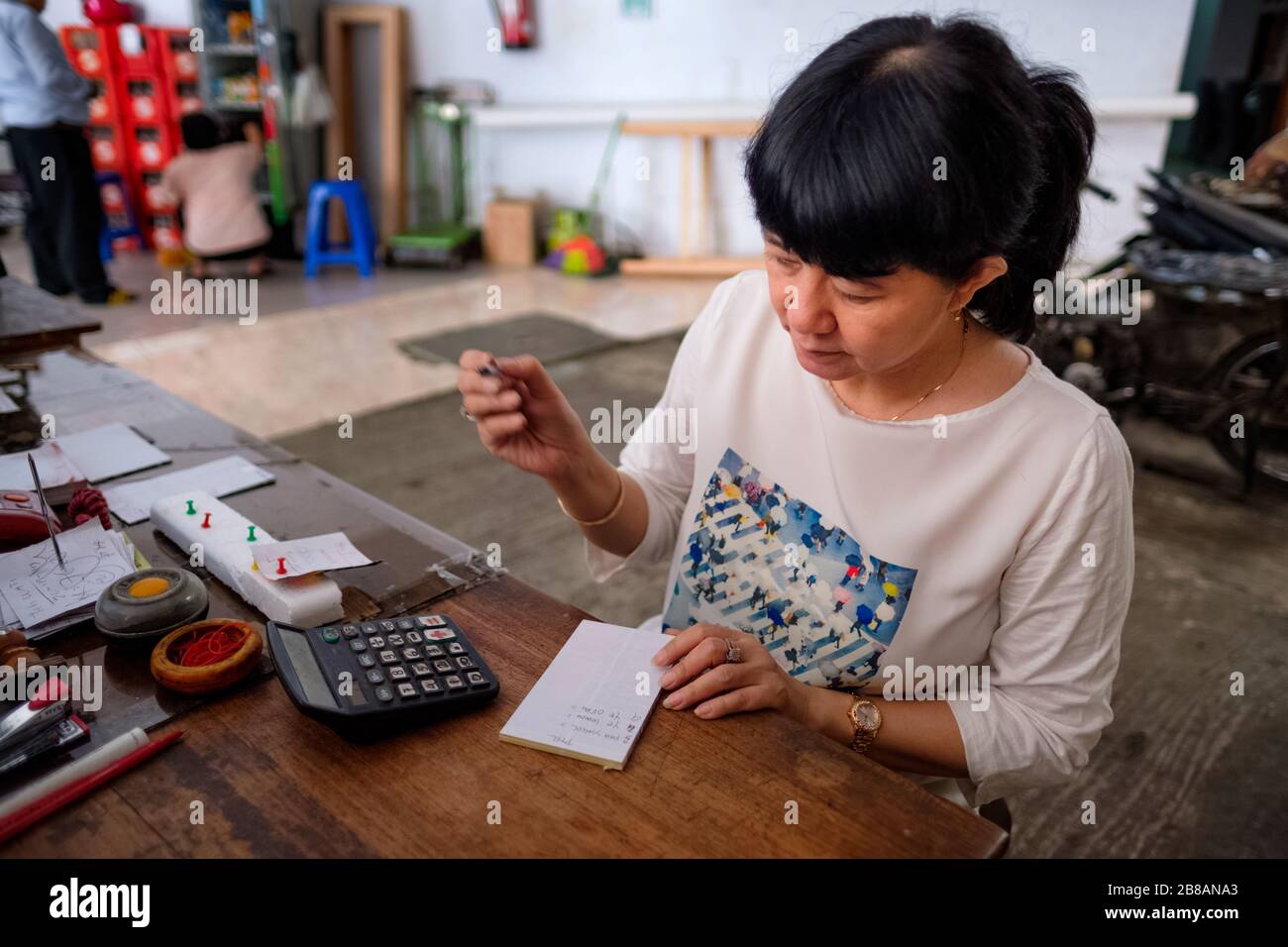 Asian Indonesian women, the owner of small local family-owned business store, or locally called warung, calculating profit by her desk. Selective Focu Stock Photo