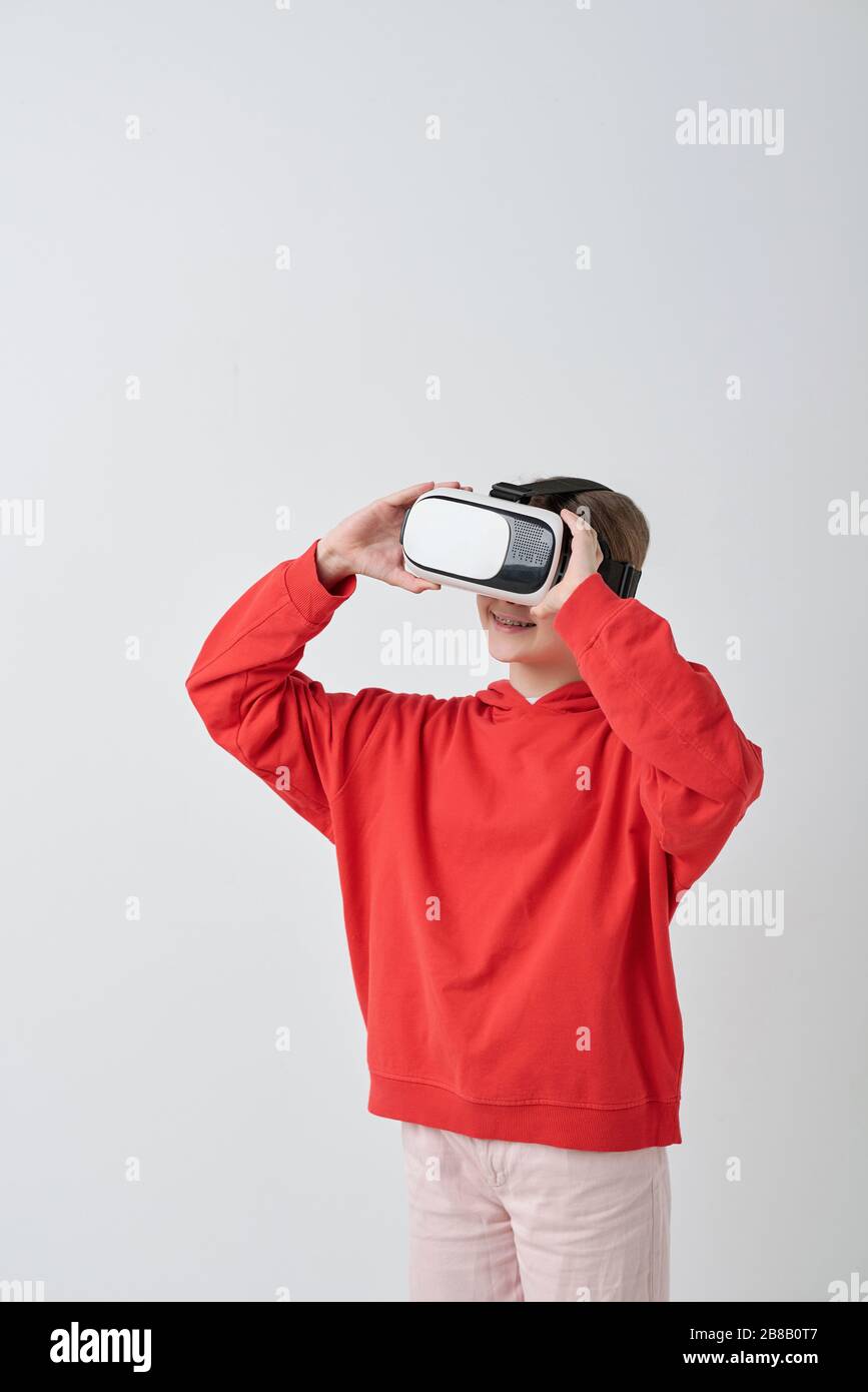 Cheerful modern teenager in casualwear watching video in vr headset while standing against white background in isolation Stock Photo