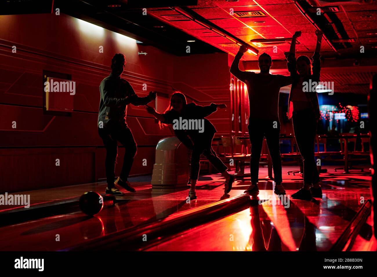 Outlines of four active friends expressing gladness while one of them throwing bowling ball on alley during game in lesiure center Stock Photo