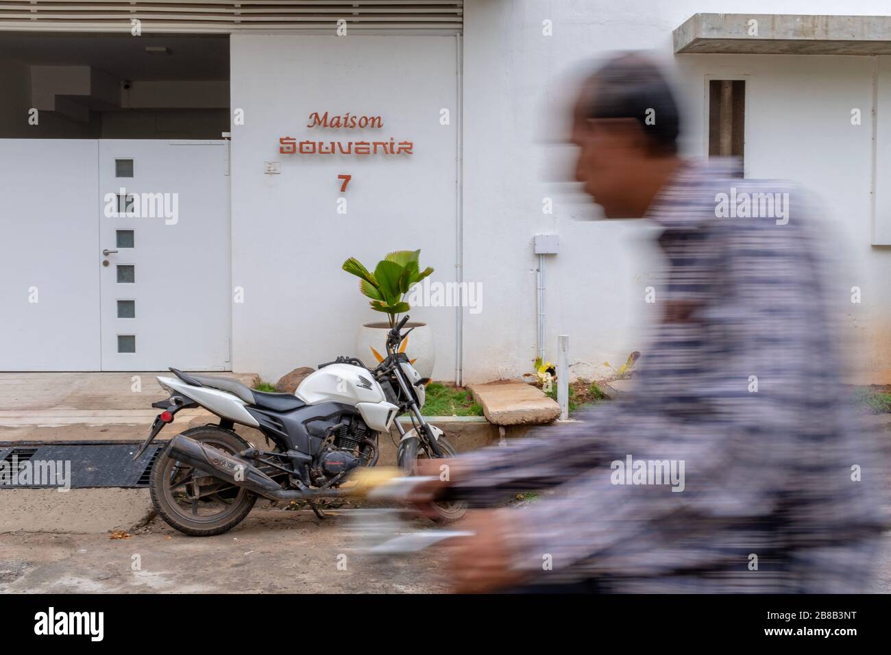 Pondicherry, India - March 17, 2018: An unrecognisable man passing in front of a nice residential building entrance on a bicycle with motion blur Stock Photo
