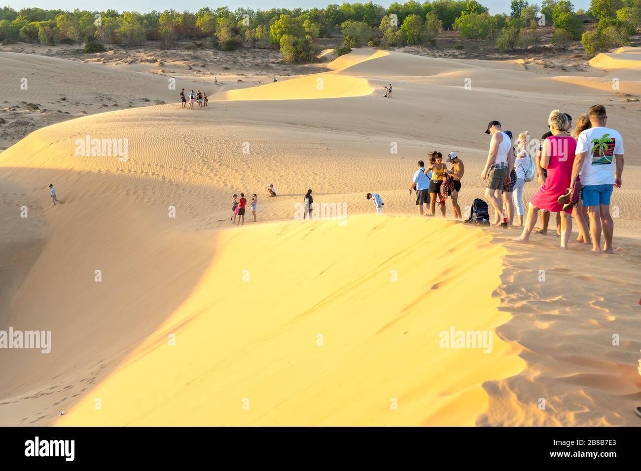 Foreign tourists experiencing the high golden sand hill to watch the sunset on top of desert in summer in Mui Ne, Vietnam Stock Photo