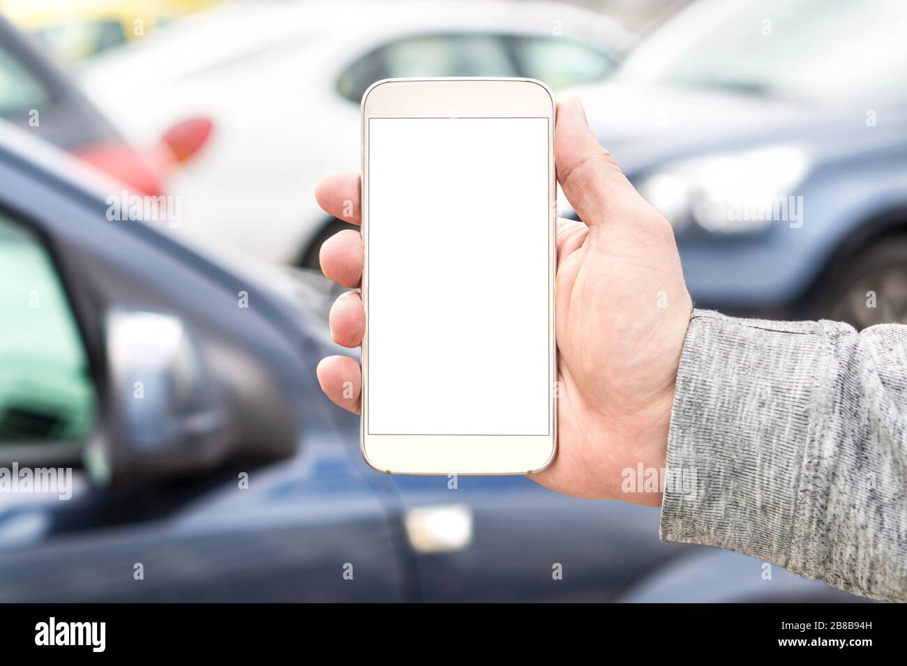 Man holding smartphone with empty blank white screen. Many cars or traffic in background. Mobile phone in hand. Template for navigation or parking. Stock Photo