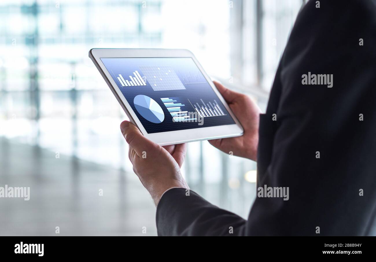 Man reading financial statistics, business graphs and trade data. Businessman using tablet in modern office building. Stock Photo