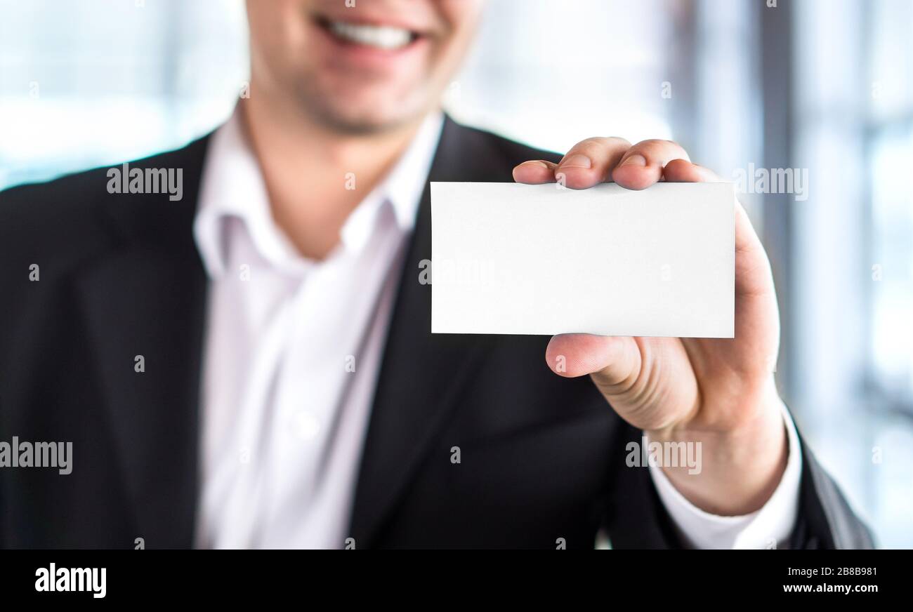 Happy smiling business man holding empty white business card in modern office building. Free blank copy space. Stock Photo
