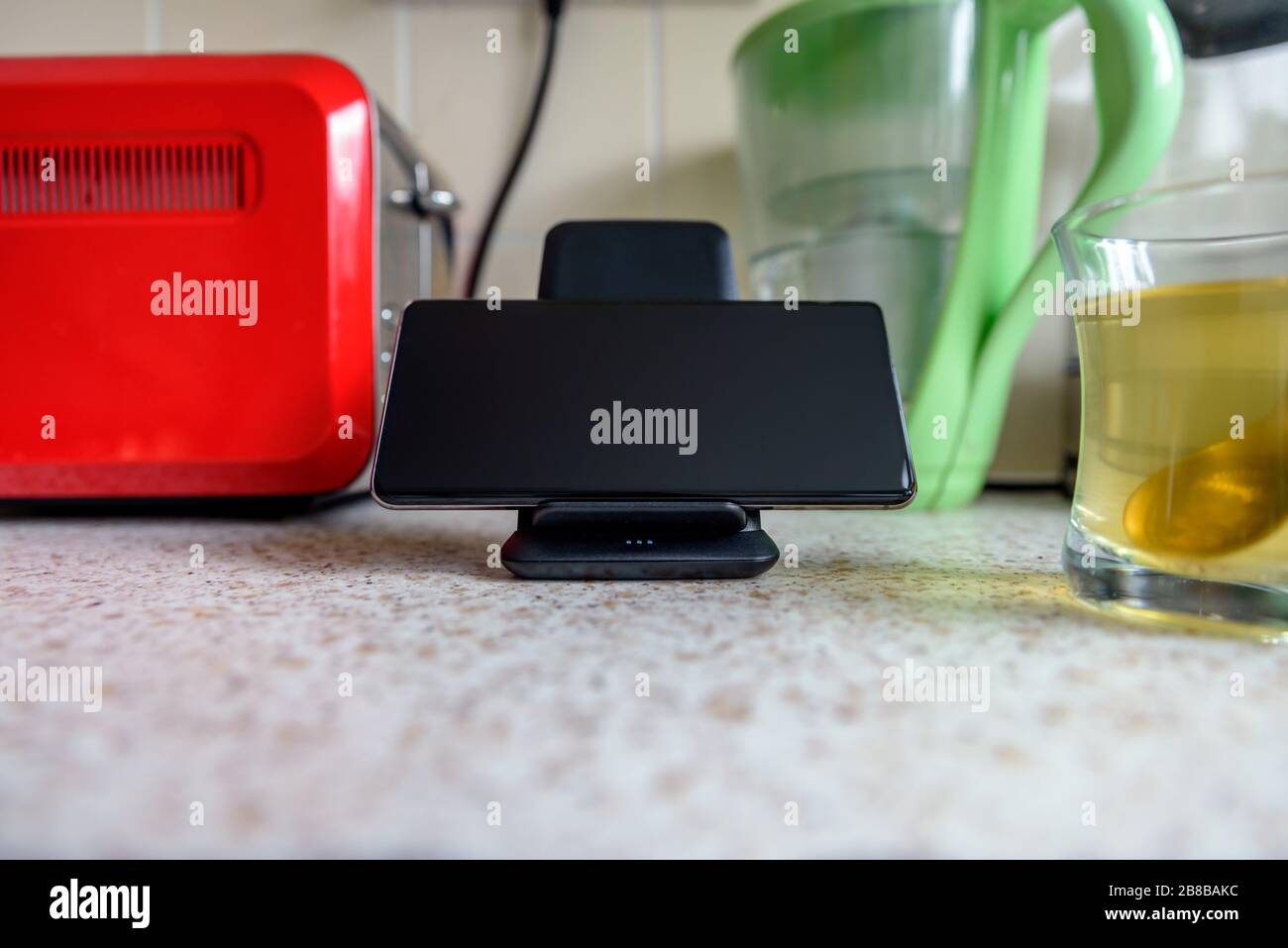 smartphone wireless charging on charging stand next to tea glass cup on ...
